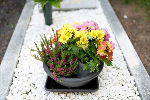a small bowl with different cemetery flowers on a grave with white pebbles