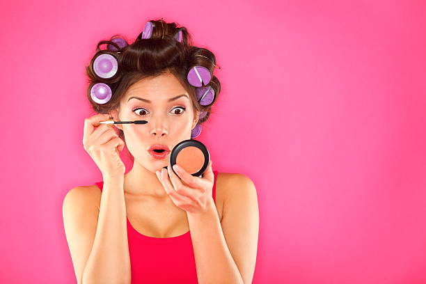 Makeup mascara woman with hair rollers Makeup mascara woman with hair rollers getting ready looking in pocket mirror. Funny image of beautiful funky trendy young mixed race asian caucasian female fashion model putting makeup on pink background. See more: curling tongs photos stock pictures, royalty-free photos & images