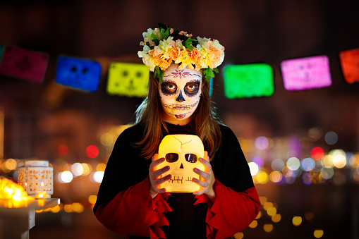 Dia de los muertos celebration. Traditional Day of the Dead party. Halloween in Mexico. Mexican girl in traditional make up and Catrina costume with a scull.