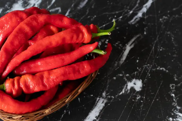 Ripe red peppers in a wicker basket placed on a dark background. A close-up. Top table view.