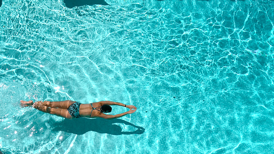 High angle view of a woman swimming face down in an outdoor pool on a sunny day