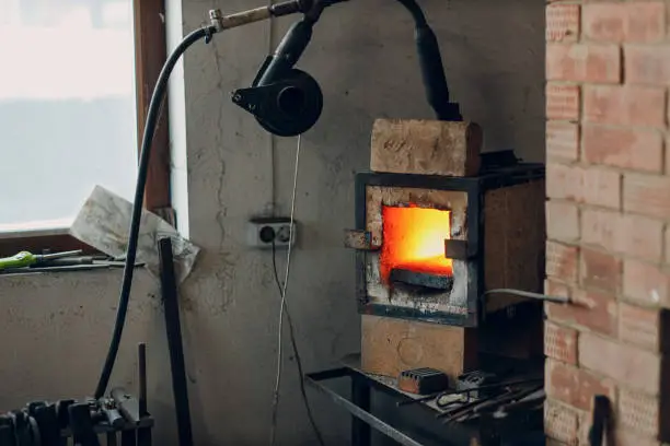 Blacksmith forge oven with hot flame. Smith heating iron piece of steel in fire of red-hot forge.