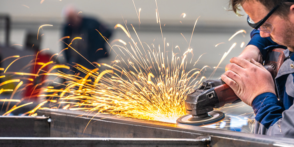 Close-up shot of grinding steel product. Cropped shot of worker operating with electric hand tool, traces of hot sparks flying away. People working in engineering industrial production.