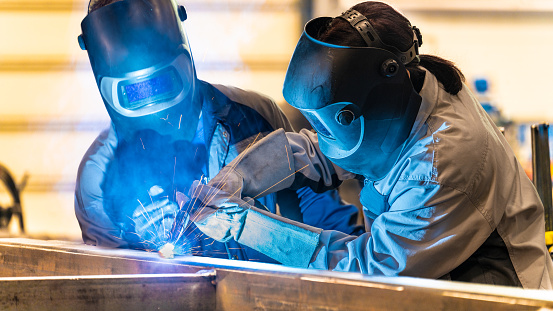 Workers welding metal material. Using protective equipment, fireproof gloves and welding helmet. People working in engineering industrial production.