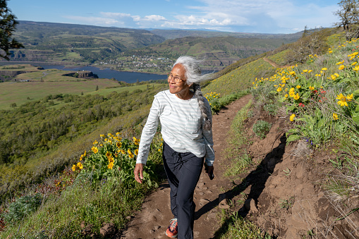 An active senior woman of Chinese and Hawaiian ethnicity is happily hiking on a sunny day. She is smiling and enjoying retirement.