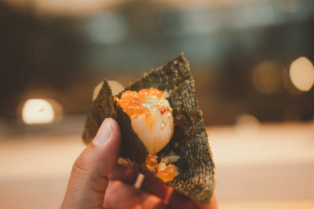 Scallop sashimi topping red salmon caviar put on seaweed sheet in hand. Scallop sashimi topping red salmon caviar put on seaweed sheet in hand ready to eat fusion food stock pictures, royalty-free photos & images