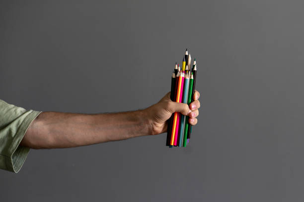 istock a person's hand holding many colorful pencils crayons 1423794157