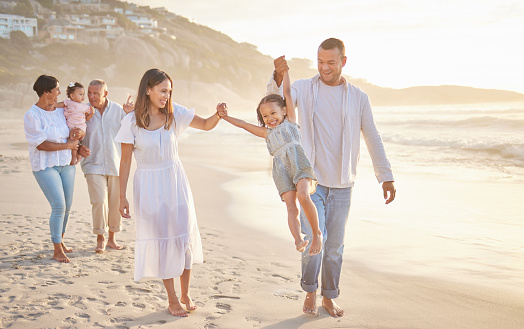 Cute little girl swinging while holding hands with her parents. Young mom and dad walking hand in hand with their daughter and lifting her while walking on the beach. Family fun in the summer sun