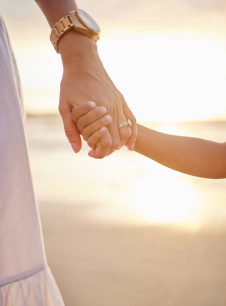 istock Closeup of unknown mixed race mother holding her little son or daughter's hand while bonding together on the beach at sunset. Hispanic child showing trust in single mother. Loving and caring parent 1423801666
