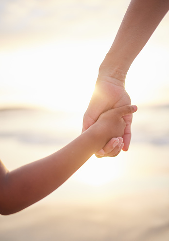 Closeup of unknown mixed race mother holding her little son or daughter's hand while bonding together on the beach at sunset. Hispanic child showing trust in single mother. Loving and caring parent