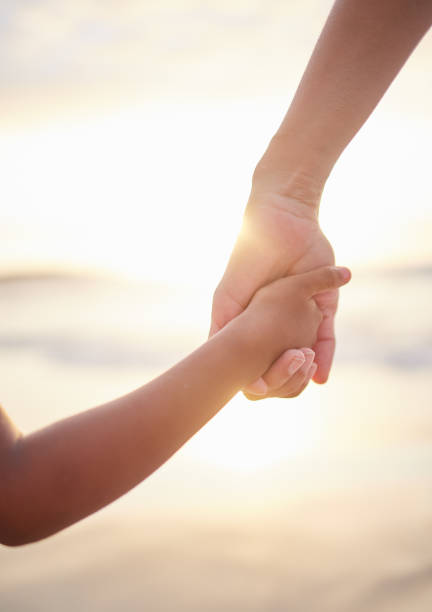 Closeup of unknown mixed race mother holding her little son or daughter's hand while bonding together on the beach at sunset. Hispanic child showing trust in single mother. Loving and caring parent Closeup of unknown mixed race mother holding her little son or daughter's hand while bonding together on the beach at sunset. Hispanic child showing trust in single mother. Loving and caring parent kids holding hands stock pictures, royalty-free photos & images