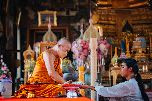 Bangkok, Thailand - August  29, 2022 .Tourist being blessed by buddhist monk inside the beautiful Wat Arun Temple in Bangkok, Thailand.