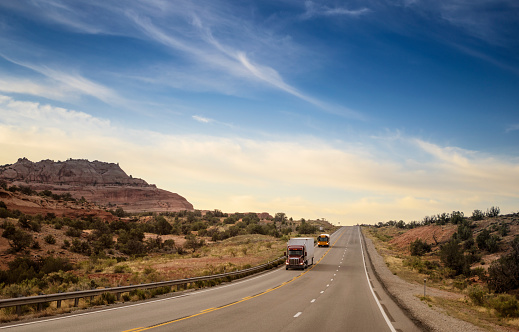 Semi truck followed by a school bus driving on an empty highway in Utah, USA