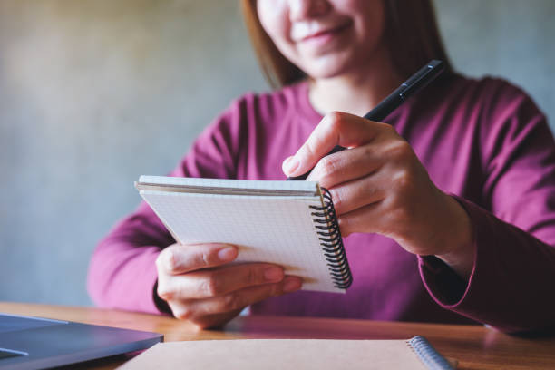 istock Closeup image of a young woman writing on a notebook while working on laptop computer 1423832272