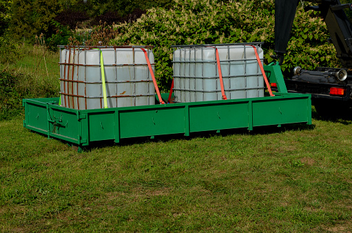 two plastic containers in a metal cage. full of water for watering or drinking livestock in hot weather. the car pulls the container onto the rear wheel. arrange a delivery of chemicals or fuel. agro , ibc container, convoy