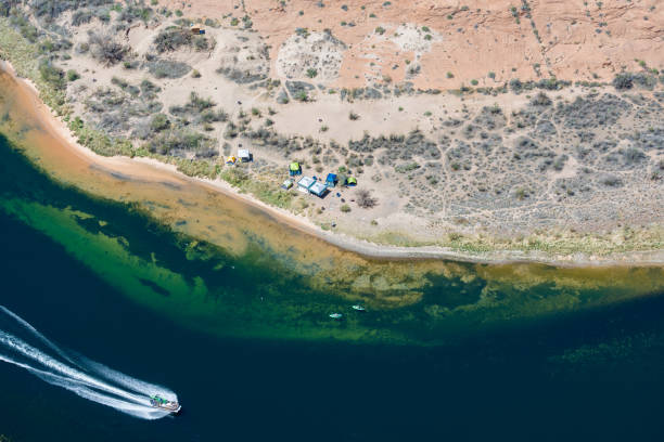 Dramatic landscape at the Grand Canyon National Park where the Colorado River runs through rock formations of eroded sand stone. People are camping on the beach at the bottom of the canyon while a speedboat is passing by.