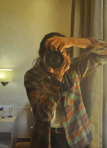A male photographer taking selfie with his DSLR camera in front of mirror inside the bedroom.
