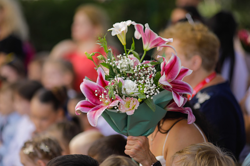Shallow depth of field (selective focus) details with a woman holding flowers during the first day of school for her child.