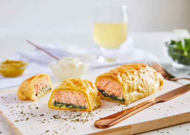 Homemade salmon strudel on table Homemade salmon strudel with spinach, served on wood board, white background with setting and ingredient fish pie stock pictures, royalty-free photos & images
