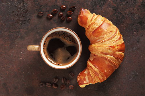 Croissant and cup of coffee on old rusty iron background, top view
