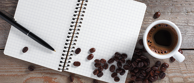 Notepad with pen and a cup of coffee on old wooden background, top view