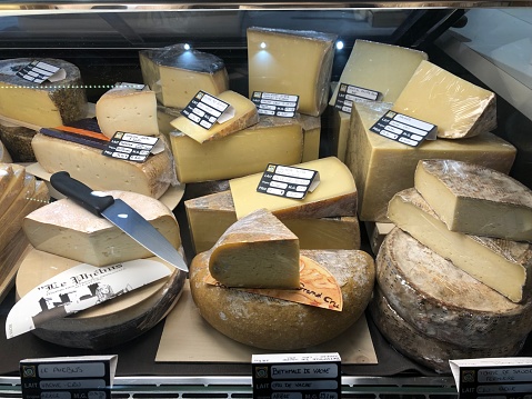Horizontal high angle closeup photo of a variety of cheeses on display on a stall at the daily indoor food market in the Old Town centre of historic city La Rochelle, Charente-Maritime, Nouvelle Aquitaine, France. 6th April, 2019