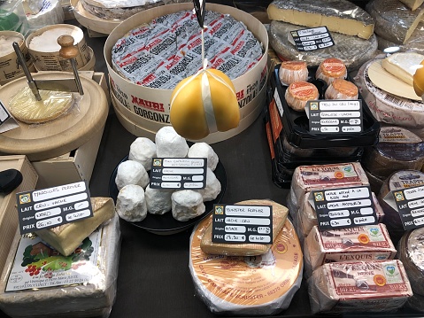 Horizontal high angle photo of a variety of cheeses and cheese products on a stall at the daily indoors food market. La Rochelle, Charente-Maritime, Nouvelle Aquitaine. \n6th April, 2019