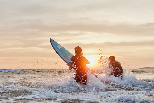 Back view of carefree surfers rushing into sea at sunset. Copy space.