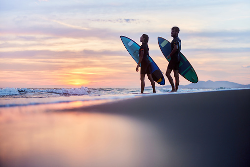 Happy couple of surfers with their surfboards during summer sunset on the beach. Copy space.