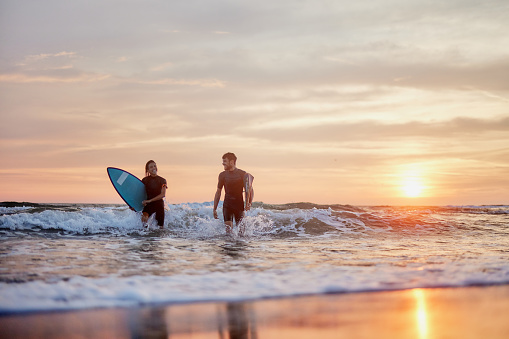 Happy couple of surfers talking while getting out of sea at sunset. Copy space.