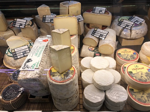 Horizontal high angle closeup photo of a large variety of cheese on display on a market stall at the daily indoor food market. La Rochelle, Charente-Maritime, Nouvelle Aquitaine. 3rd May 2019