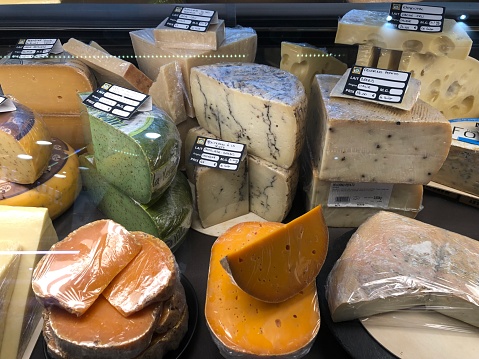 Horizontal high angle closeup photo of a variety of cheeses on a market stall at the daily indoor Food Market in the historic city of La Rochelle, Charente-Maritime, Nouvelle Aquitaine, France. 3rd May, 2019.