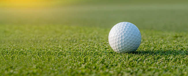 A golf ball on the putting green at sunset.