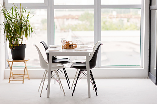Modern interior of a cozy dining room kitchen, white furniture, against the background of a panoramic window. Conceptual decor design, house mortgage loan for a young family. Soft selective focus.