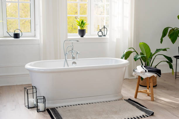 istock Stylish modern bathroom interior. Horizontal view of an empty free-standing bathtub on a wooden floor in a bright room against the backdrop of a large window and houseplants. Soft selective focus. 1423854654