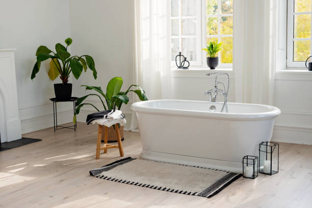 istock Stylish modern bathroom interior. Horizontal view of an empty free-standing bathtub on a wooden floor in a bright room against the backdrop of a large window and houseplants. Soft selective focus. 1423854659