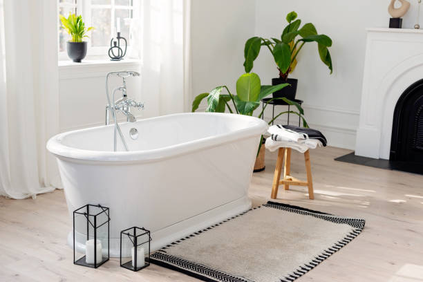 istock Stylish modern bathroom interior. Horizontal view of an empty free-standing bathtub on a wooden floor in a bright room against the backdrop of a large window and houseplants. Soft selective focus. 1423854671