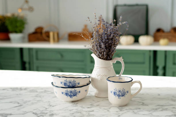 A bouquet of lavender and a set of white dishes: a porcelain milk jug, a coffee cup and bowls on a white countertop against a green kitchen. Soft selective focus. A bouquet of lavender and a set of white dishes: a porcelain milk jug, a coffee cup and bowls on a white countertop against a green kitchen. Soft selective focus. plate rack stock pictures, royalty-free photos & images