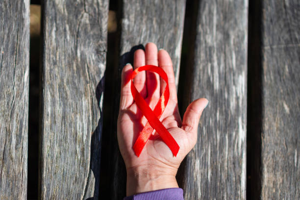 Female hand holding red ribbon HIV, AIDS awareness ribbon.World Aids Day concept. Woman's hand support for World aids day and national HIV,AIDS concept.Wooden surface.Top view. mano femenina sosteniendo cinta roja vih, cinta de concientización sobre el sida. concepto del día mundial del sida. apoyo de la mano de la mujer para el día mundial del sida y el concepto nacional de vih,sida. superficie de madera. vista superior.