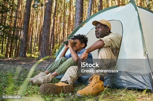 istock Cute African American boy looking through binoculars while sitting in tent 1423865834