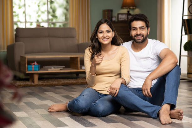 young couple sitting on floor, stock photo - pointing women cheerful front view imagens e fotografias de stock