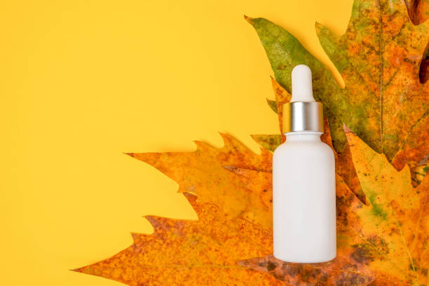 istock White cosmetic dropper bottle with dry falling leaves on yellow background. Autumn composition. Concept of natural and organic skincare products 1423867861