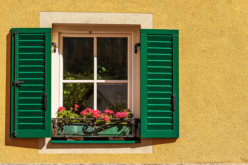 Close-up of a window with green wooden shutters and red geranium flowers. Small village of Malborghetto-Valbruna in Val Canale, Udine province, Friuli-Venezia Giulia, Italy, Europe.