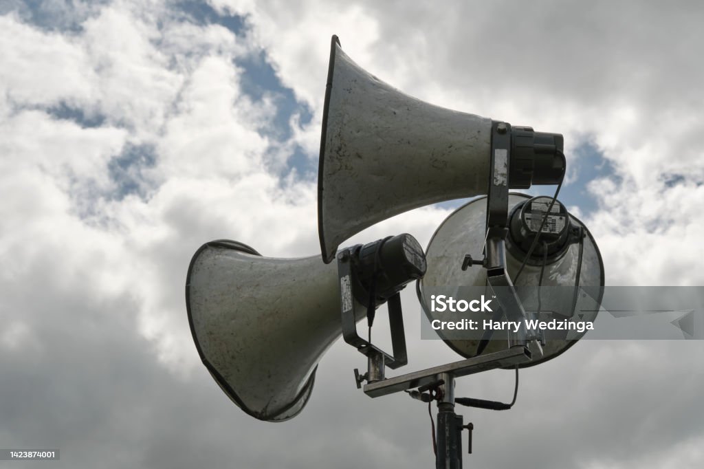 Three large old metal megaphones Three large old metal megaphones or loudspeakers against a dramatic cloudy sky. Air Raid Siren Stock Photo