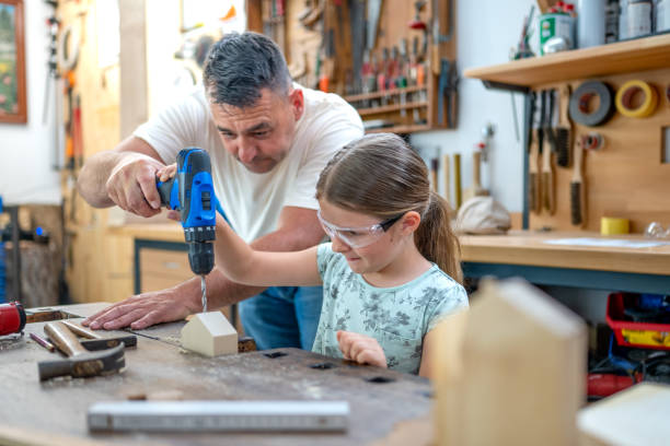 Girl and father drilling hole into small wooden house stock photo