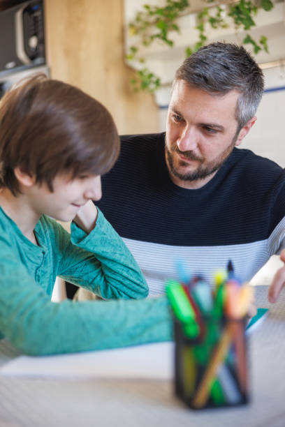 istock Man sitting with preadolescent boy and assisting him in doing homework 1423881776