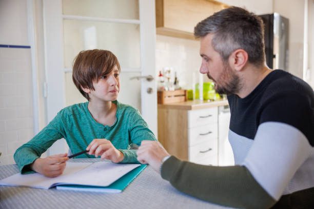 istock Preadolescent boy sitting at home and doing homework with his caretaker 1423881807