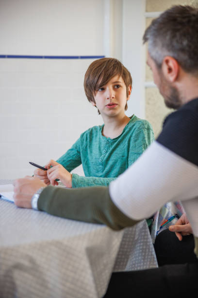 istock Preadolescent boy sitting at the table and talking to his caretaker 1423881840