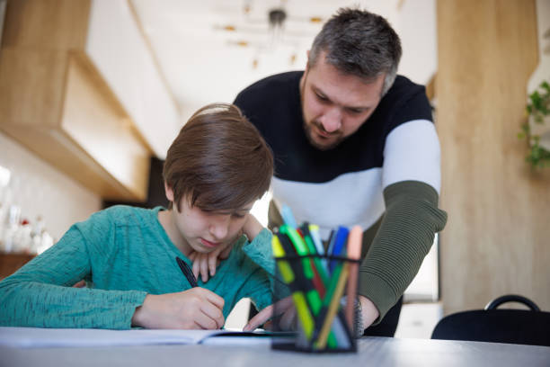 istock Man standing by the table and supervising boy who is doing homework at home 1423881877