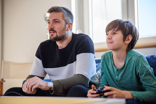 Preadolescent boy sitting on the sofa with his caretaker and playing video games at home